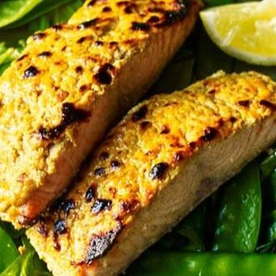 Golden-brown, spice-coated grilled food pieces arranged over glossy green leaves.