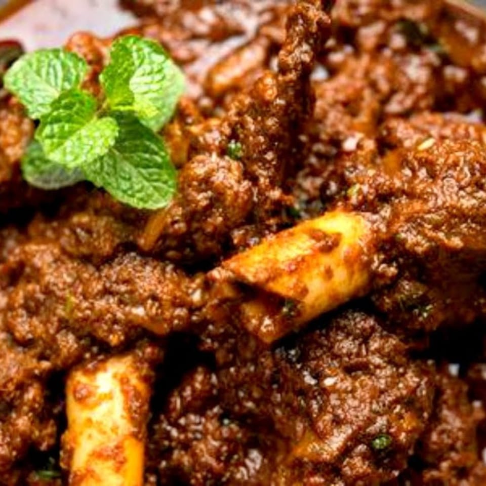 Close-up of roasted meat pieces garnished with fresh mint leaves and orange slices.