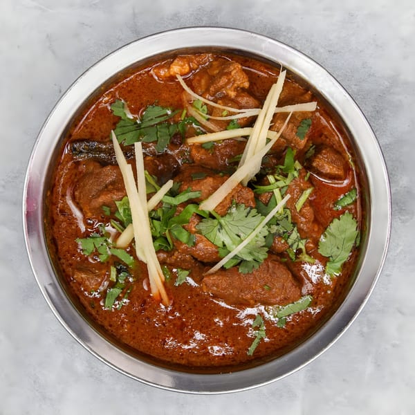 Chakra Indian Cuisine's lamb curry, garnished with fresh cilantro and ginger, in a silver bowl.