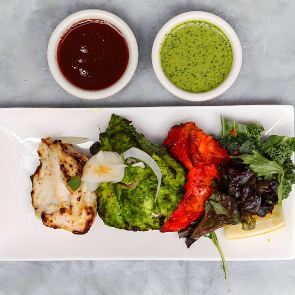 Chakra Indian Cuisine's colorful chicken tikka platter with green and red sauces, fresh greens, and lemon.