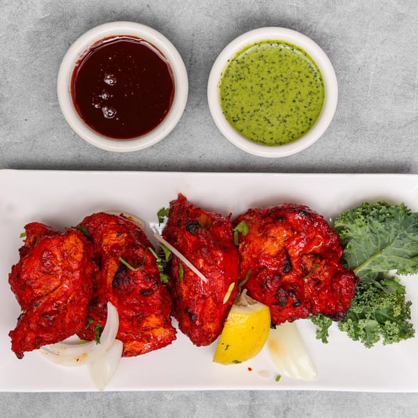 Chakra Indian Cuisine's Tandoori Chicken, served with lemon, onions, kale, and two dipping sauces.